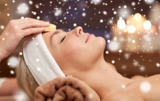 A woman's smiling face is seen during a Saybrook spa visit, with snow flurries in the forefront and background.